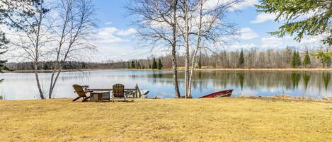 A lakeside setting with a table and chairs, a boat, and trees.