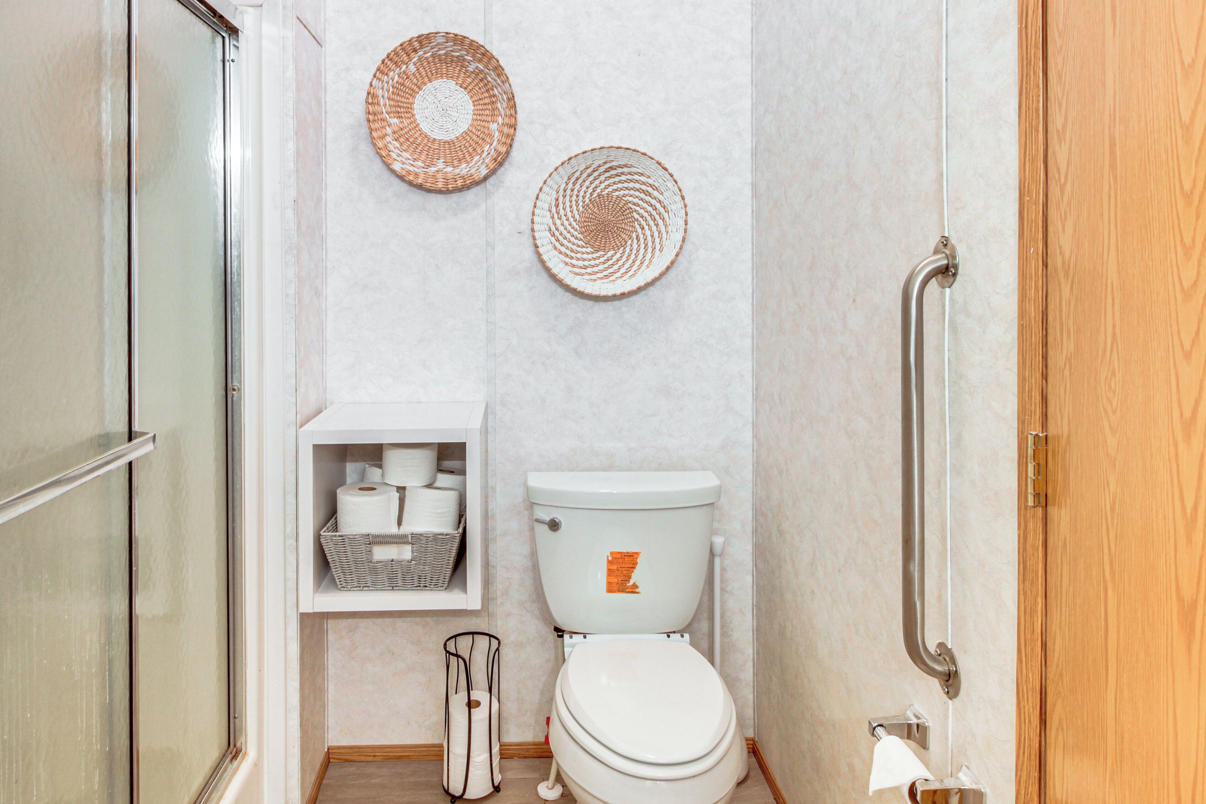 Une salle de bain avec des toilettes, une étagère contenant des articles de toilette et deux éléments de décoration murale en fibres tressées.
