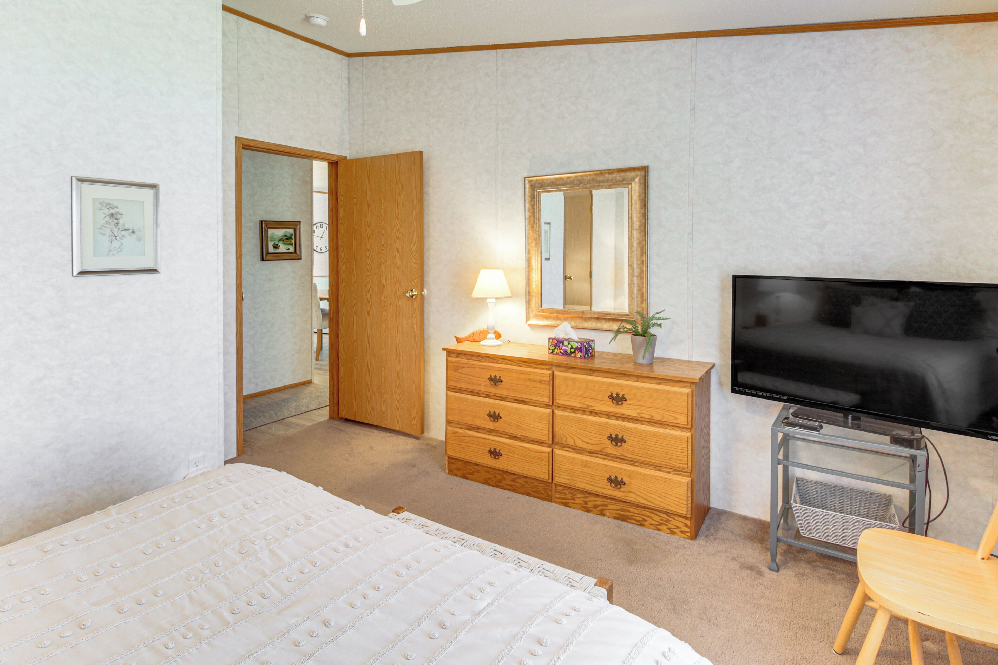 Ein Schlafzimmer mit Bett, Holzkommode, Fernseher und Spiegel.