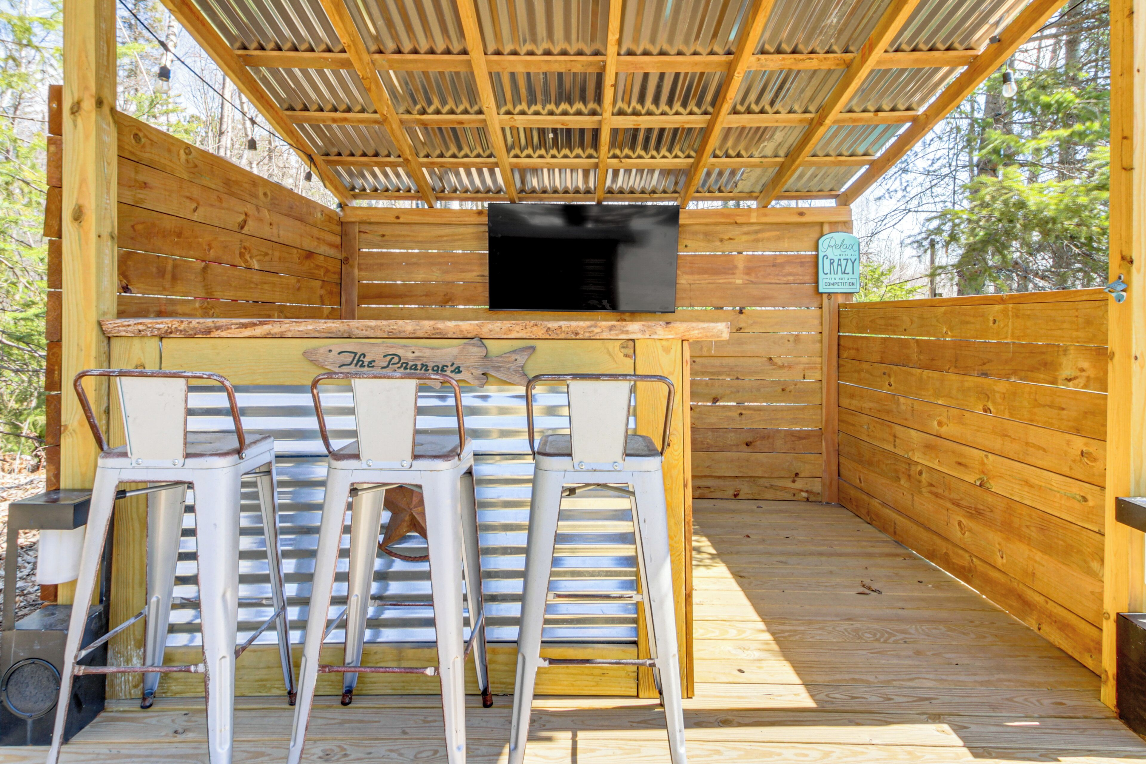 Un área de bar exterior de madera con taburetes de metal y una parrilla.