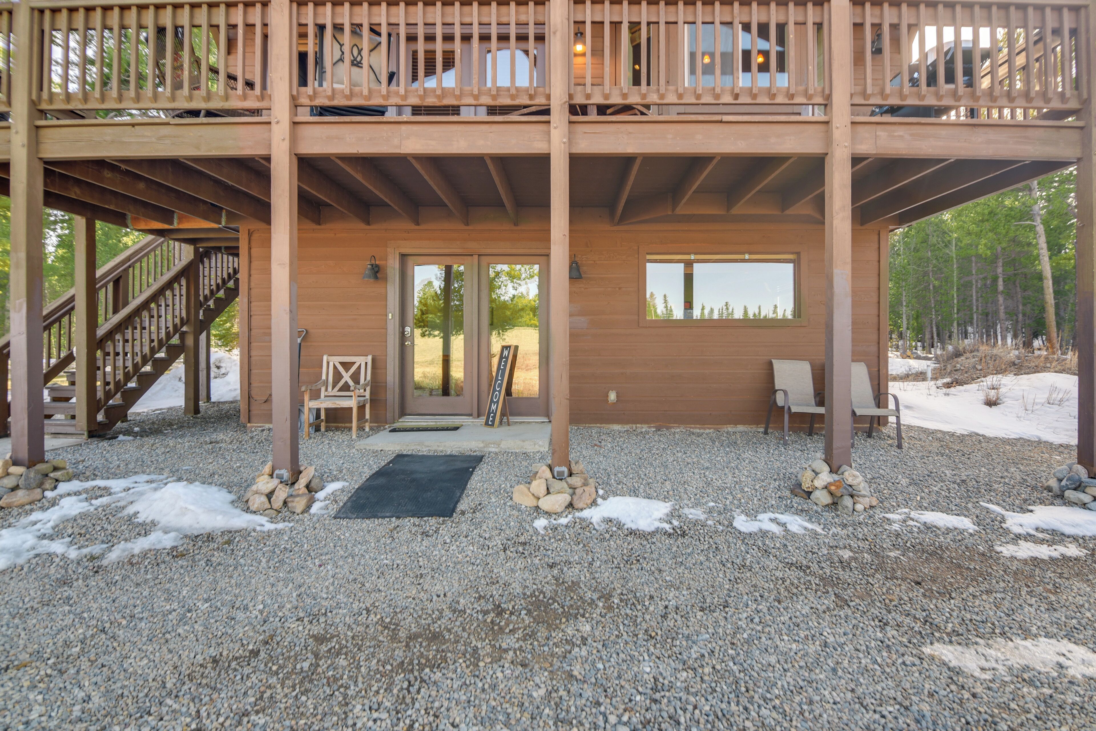 A wooden deck with a staircase leading to a second level, a door with a sign, and a view of trees.