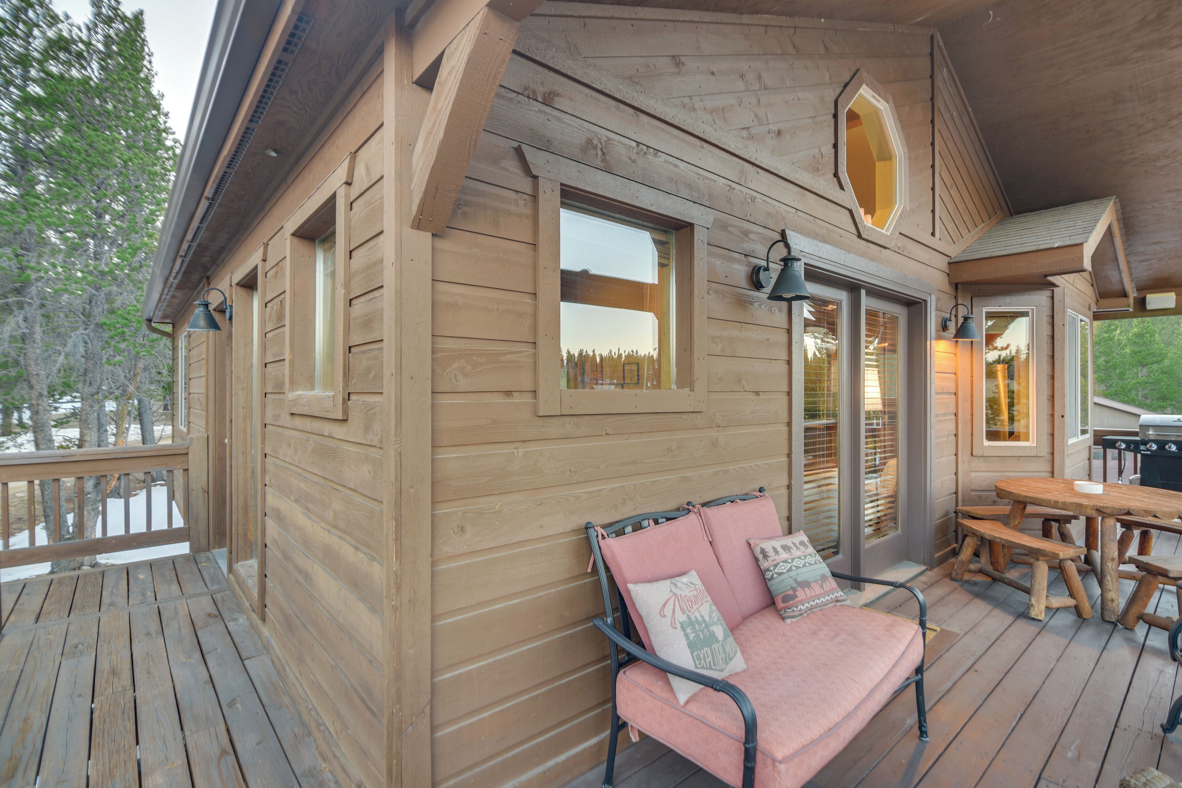 Eine Holzhütte mit einer Terrasse, einer Couch mit Kissen und einem Esstisch.