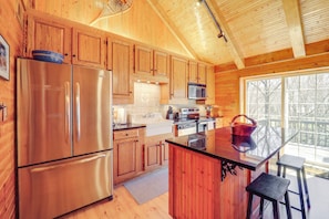 Cocina de cabaña de madera con refrigerador de acero inoxidable, armarios de madera, microondas y una isla grande con taburetes.