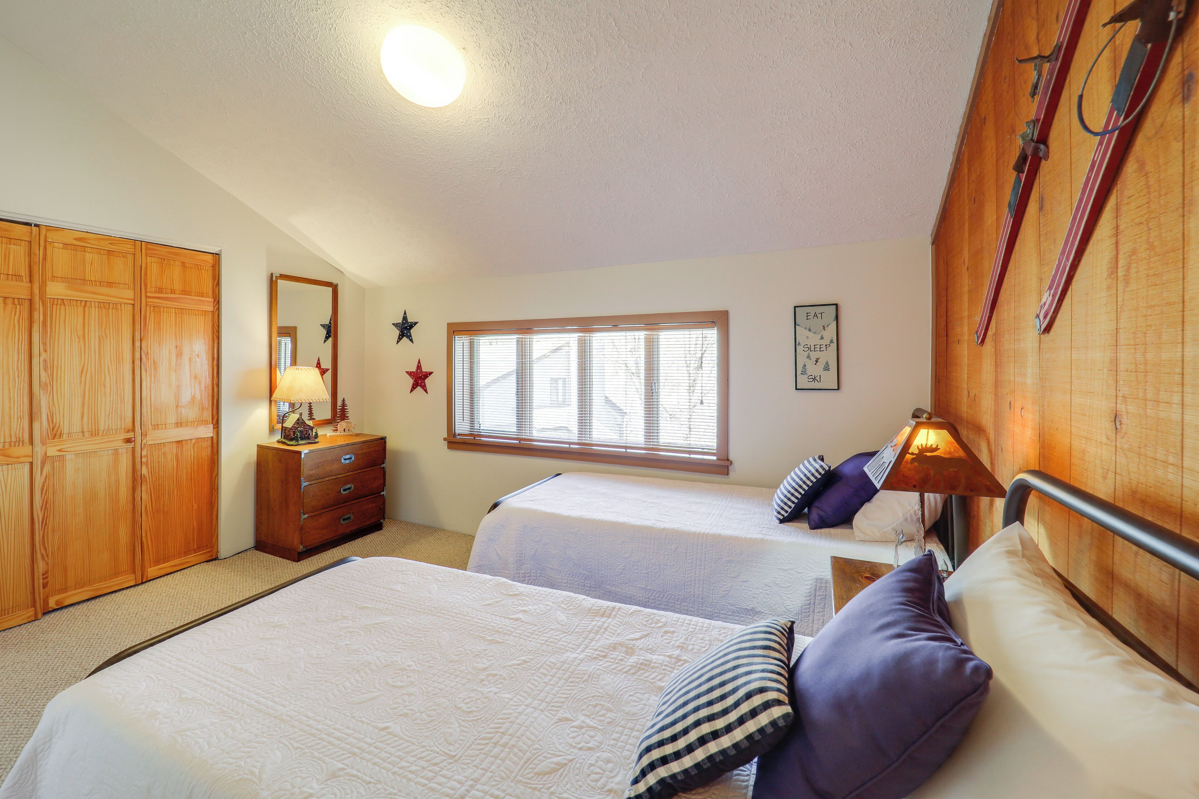 A bedroom with two beds, wooden wardrobe, dresser, window with blinds, and wall decorations.