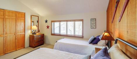 A bedroom with two beds, wooden wardrobe, dresser, window with blinds, and wall decorations.