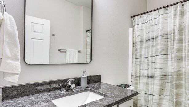 A bathroom with a white sink, a mirror, a towel hanging on the wall, and a shower curtain. - Military-friendly Home Near Navarre Beach & Base! (Mary Esther)