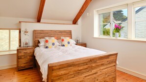 Un dormitorio con cama de madera, paredes blancas, una ventana con vistas y techo de madera.