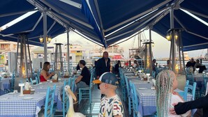An outdoor dining area with blue tables and chairs, a large bird, and people dining. - Celeste by the Sea: Summer Chill, Pool, Beach 2BR. (Paphos)