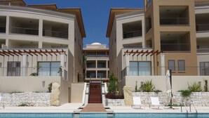 A hotel with a central pool, multiple balconies, and a stone facade. - Celeste by the Sea: Summer Chill, Pool, Beach 2BR. (Paphos)