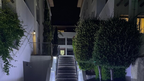 A nighttime view of a building's entrance with a staircase leading up to a door, surrounded by greenery and illuminated by underglow lighting. - Celeste by the Sea: Summer Chill, Pool, Beach 2BR. (Paphos)