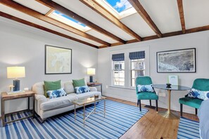 Un salon comprenant un canapé, deux fauteuils, une table basse, une carte accrochée au mur et une lucarne.