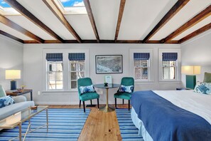 Une chambre à coucher avec un grand lit, deux chaises, une petite table et une fenêtre donnant sur un beau paysage.