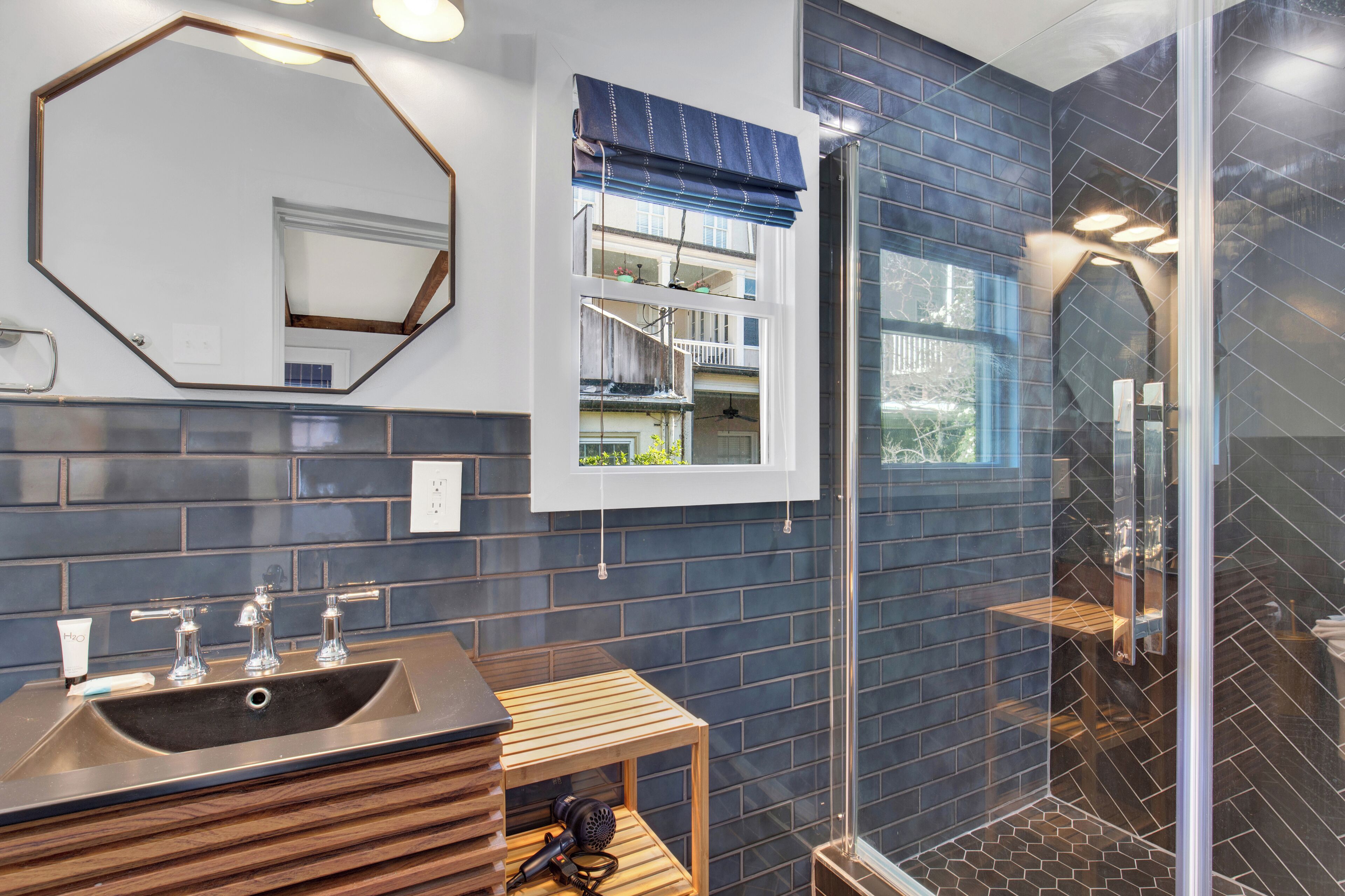 A bathroom with a large mirror, a sink with three faucets, a window with a view of a balcony, and a glass shower enclosure.