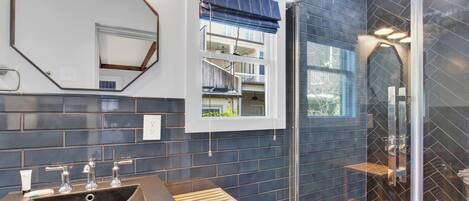 A bathroom with a large mirror, a sink with three faucets, a window with a view of a balcony, and a glass shower enclosure.