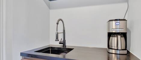 Una cocina con encimera negra, cafetera de acero inoxidable y un grifo moderno.