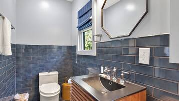 A modern bathroom with a toilet, sink, and window with blue blinds.