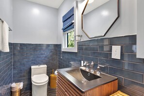 Une salle de bain moderne équipée de toilettes, d’un lavabo et d’une fenêtre avec des stores bleus.