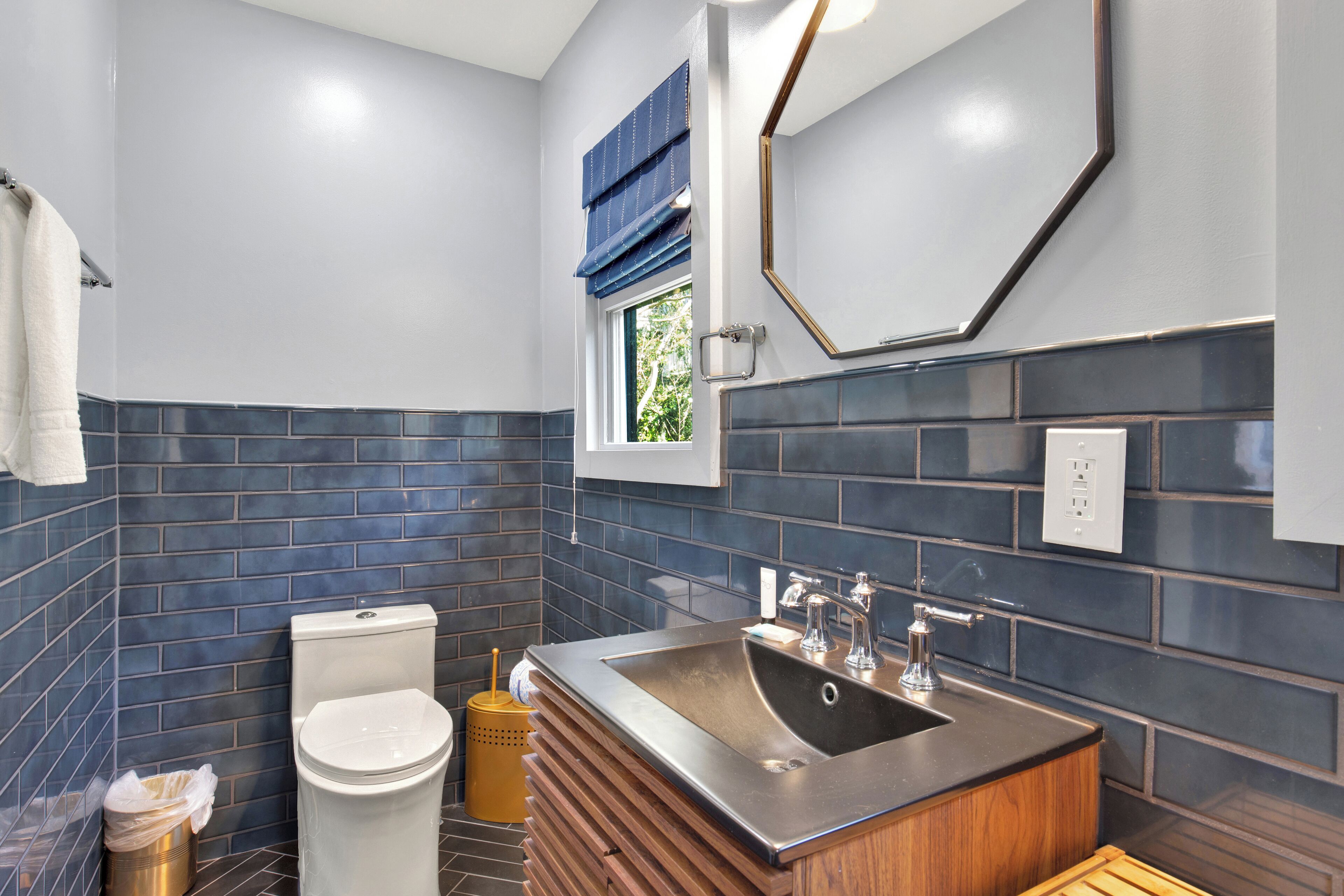 Un baño moderno con inodoro, lavamanos y ventana con persianas azules.