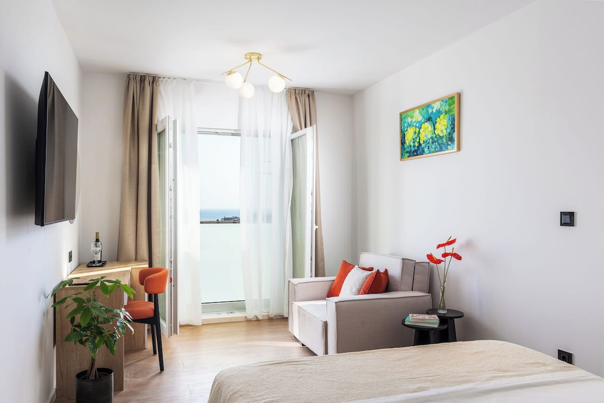 A modern hotel room with a bed, a sofa, a desk, and a potted plant.