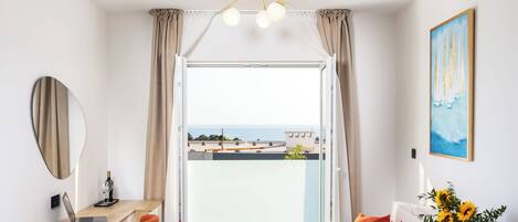 A modern room with a desk, chair, and a view of the sea through a large window.