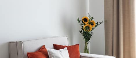 A modern living room with a sofa, a framed painting, and a vase of sunflowers.