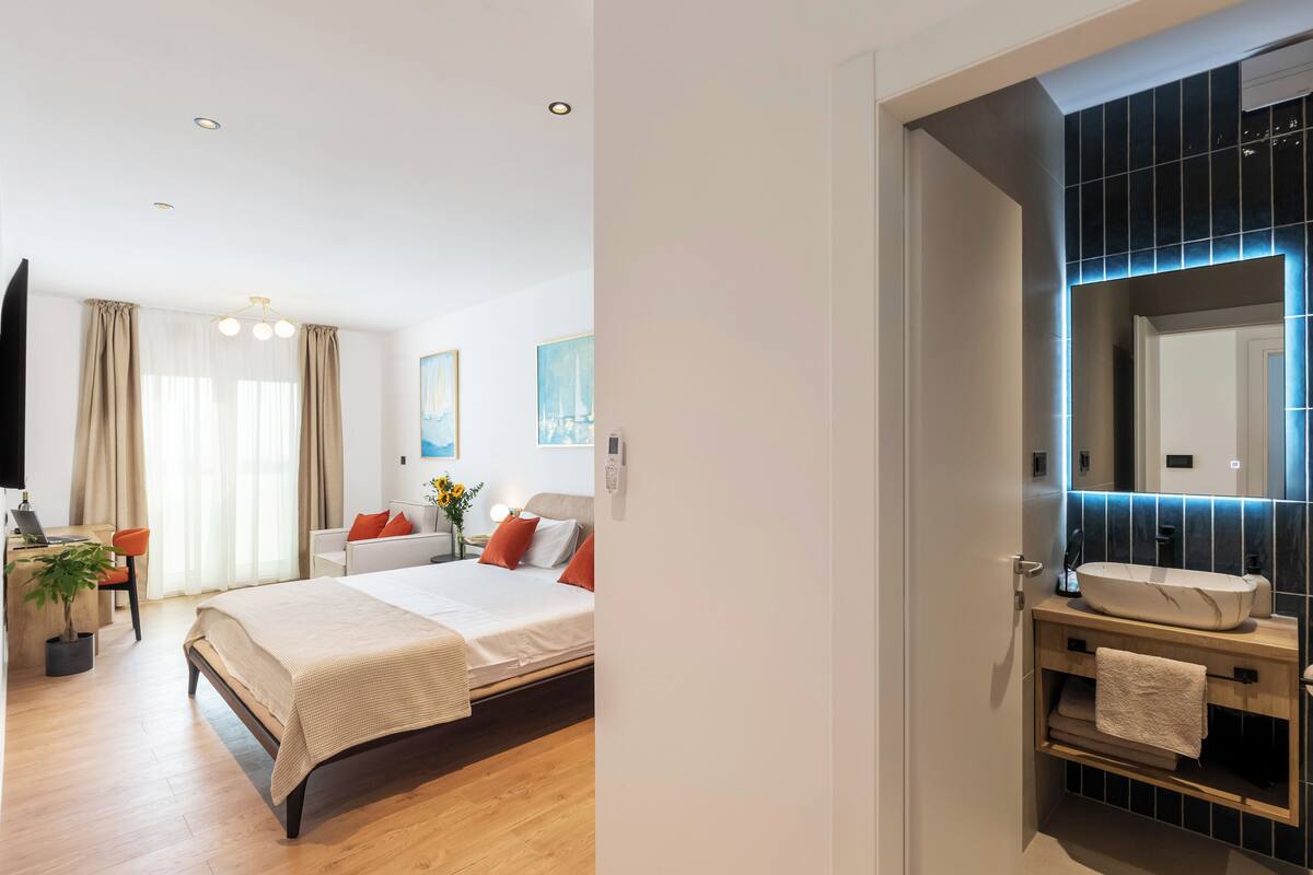 A modern hotel room with a bed, desk, and a bathroom with a large mirror and sink.