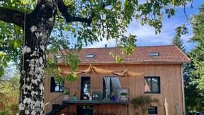 Een houten huis met een dak van rode tegels, een balkon en een trap naar de ingang.