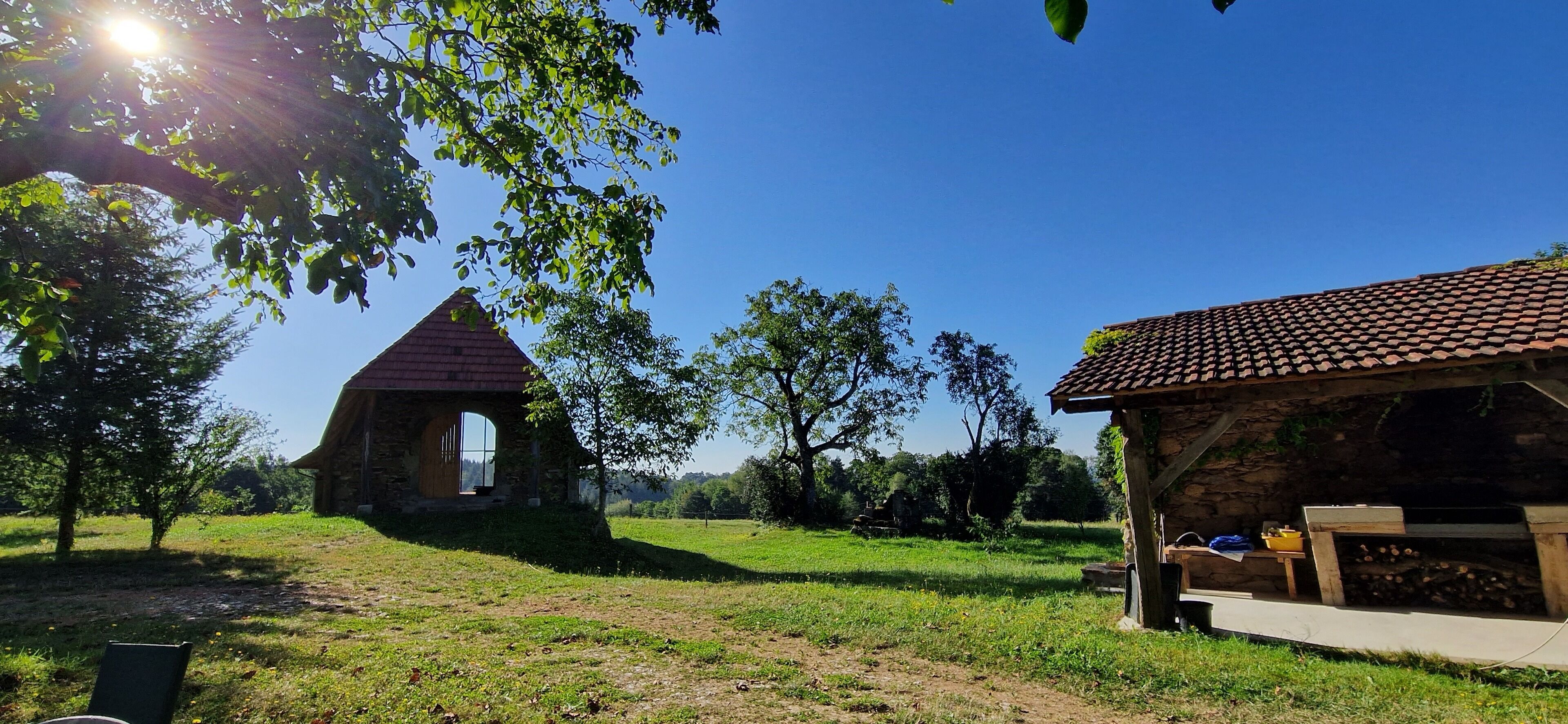 Un bâtiment rustique en pierre, avec un toit recouvert de tuiles rouges, un banc en bois et une petite table sur laquelle sont posés divers objets.