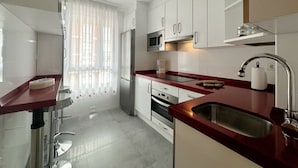 Een moderne keuken met witte kastjes, roestvrijstalen apparatuur en een rode aanrechtblad.