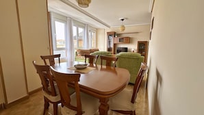 Een eethoek met een houten tafel en stoelen, een groene bank en een keuken op de achtergrond.