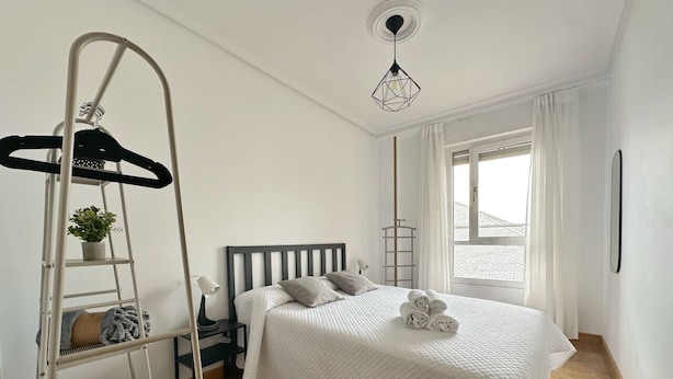 Een slaapkamer met een bed, een ladder, een nachtkastje, een lamp en een raam met gordijnen.