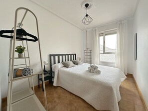 Ein Schlafzimmer mit Bett, einer Sprosse, einem Nachttisch, einer Lampe und einem Fenster mit Vorhängen.
