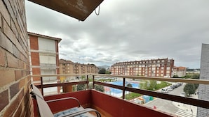 Een balkon met twee comfortabele stoelen, een bakstenen muur en uitzicht op een sportveld en gebouwen op de achtergrond.