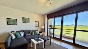 A living room with a sofa, a coffee table, and large windows offering a view of the outdoors.
