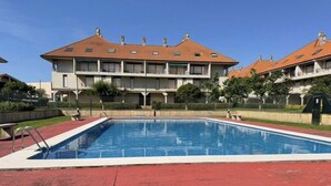 A swimming pool with a red deck, surrounded by a building with a tiled roof and multiple windows.