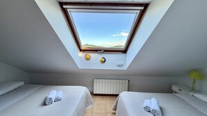 A room with two beds, a skylight, a radiator, and a small table with a lamp.