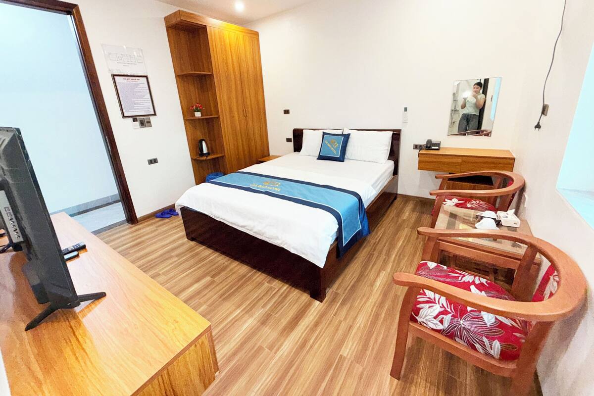 A hotel room with a bed, wooden desk, chair, and a small table.