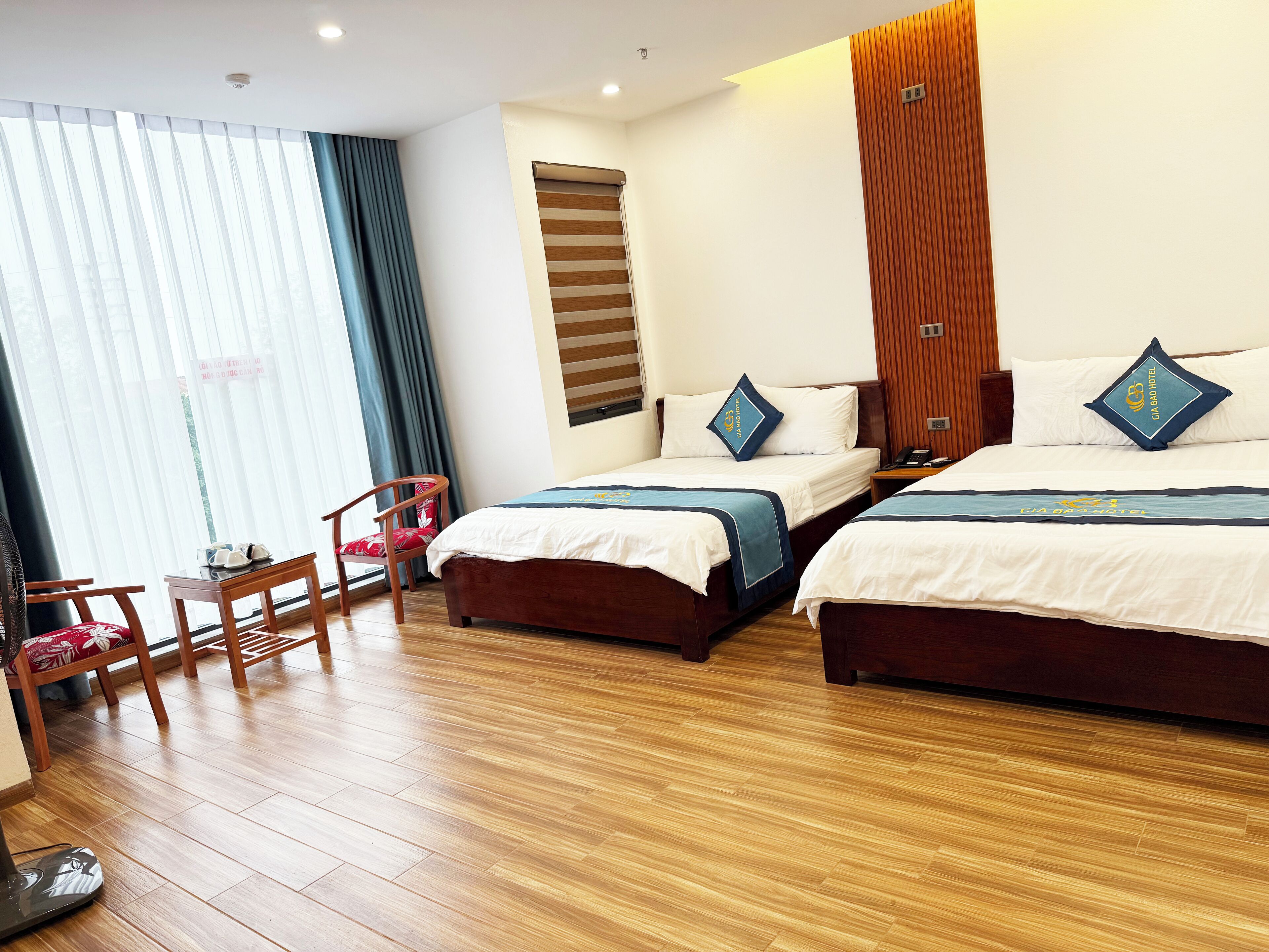 Ein Hotelzimmer mit zwei Betten, Holzboden, einem Sessel und einem Fenster mit Vorhängen.