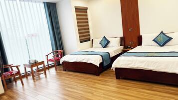 Ein Hotelzimmer mit zwei Betten, Holzboden, einem Sessel und einem Fenster mit Vorhängen.