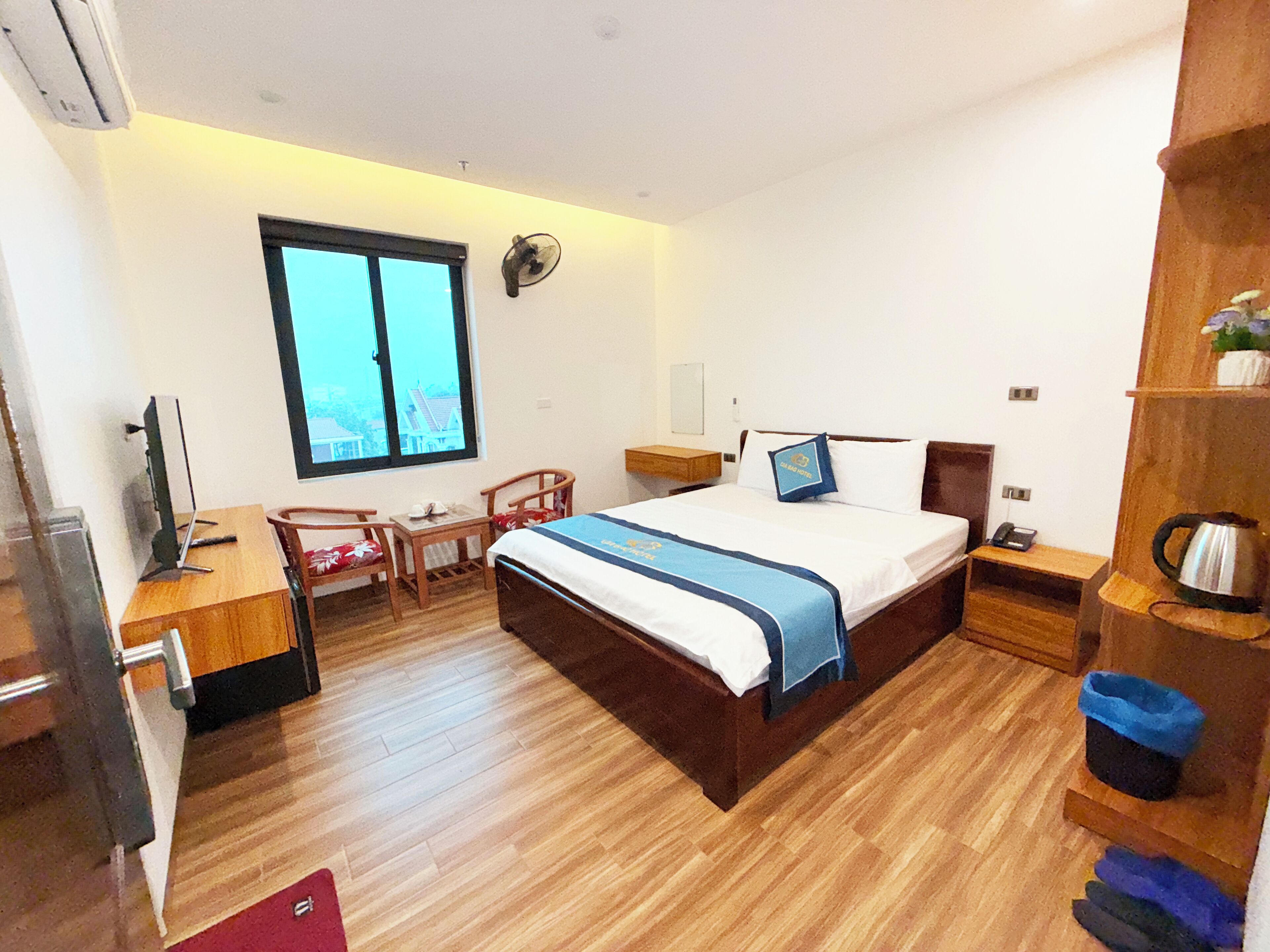 Quarto de hotel com cama, escrivaninha, cadeira e janela.