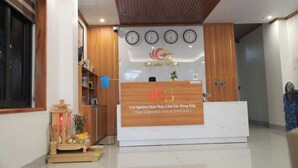A hotel reception area with a wooden reception desk, a wall clock, and a decorative item on the left. - Gia Bao Hotel Phu Tho (Van Phu)
