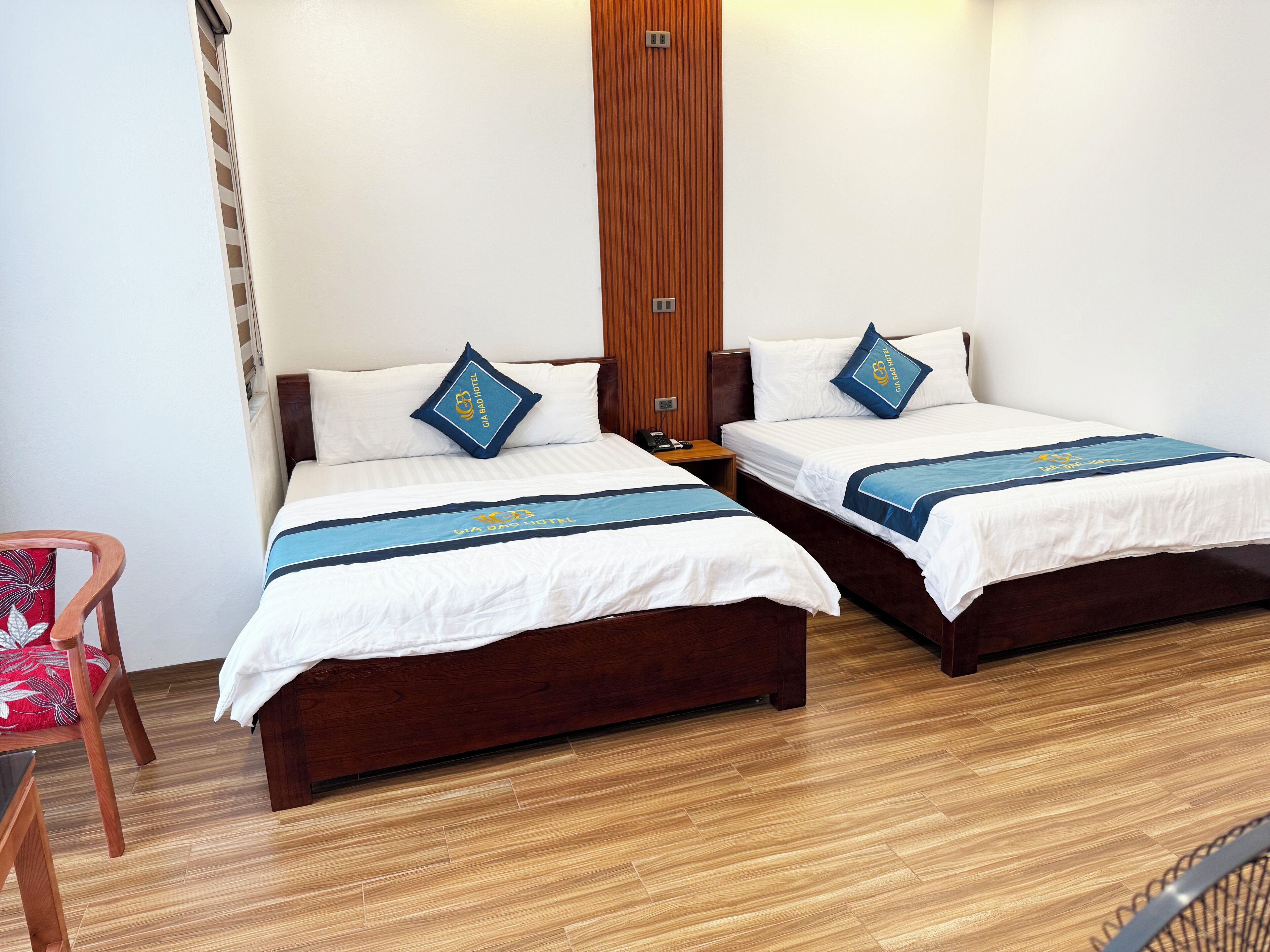 A hotel room with two wooden beds, each with a white bedspread and blue decorative pillows.