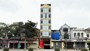 A multi-story hotel with a prominent sign, a red flag, and various storefronts along the street. - Gia Bao Hotel Phu Tho (Van Phu)