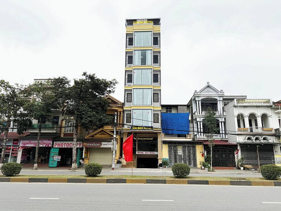 A multi-story hotel with a prominent sign, a red flag, and various storefronts along the street.
