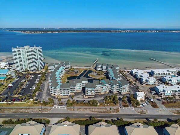 A coastal hotel complex with multiple buildings, a parking lot, and a beach view.