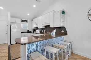 Une cuisine moderne avec des meubles blancs, un plan de travail en granit et un îlot central intégré, agrémenté de tabourets de bar.