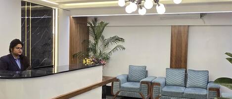 A reception area with a curved reception desk, a seating area with patterned sofas, a patterned rug, and a ceiling light fixture.