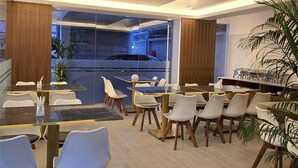 A modern dining area with glass tables and chairs, a bar, and a view of the street. - Royal Regent Suites Dhaka (Dhaka)