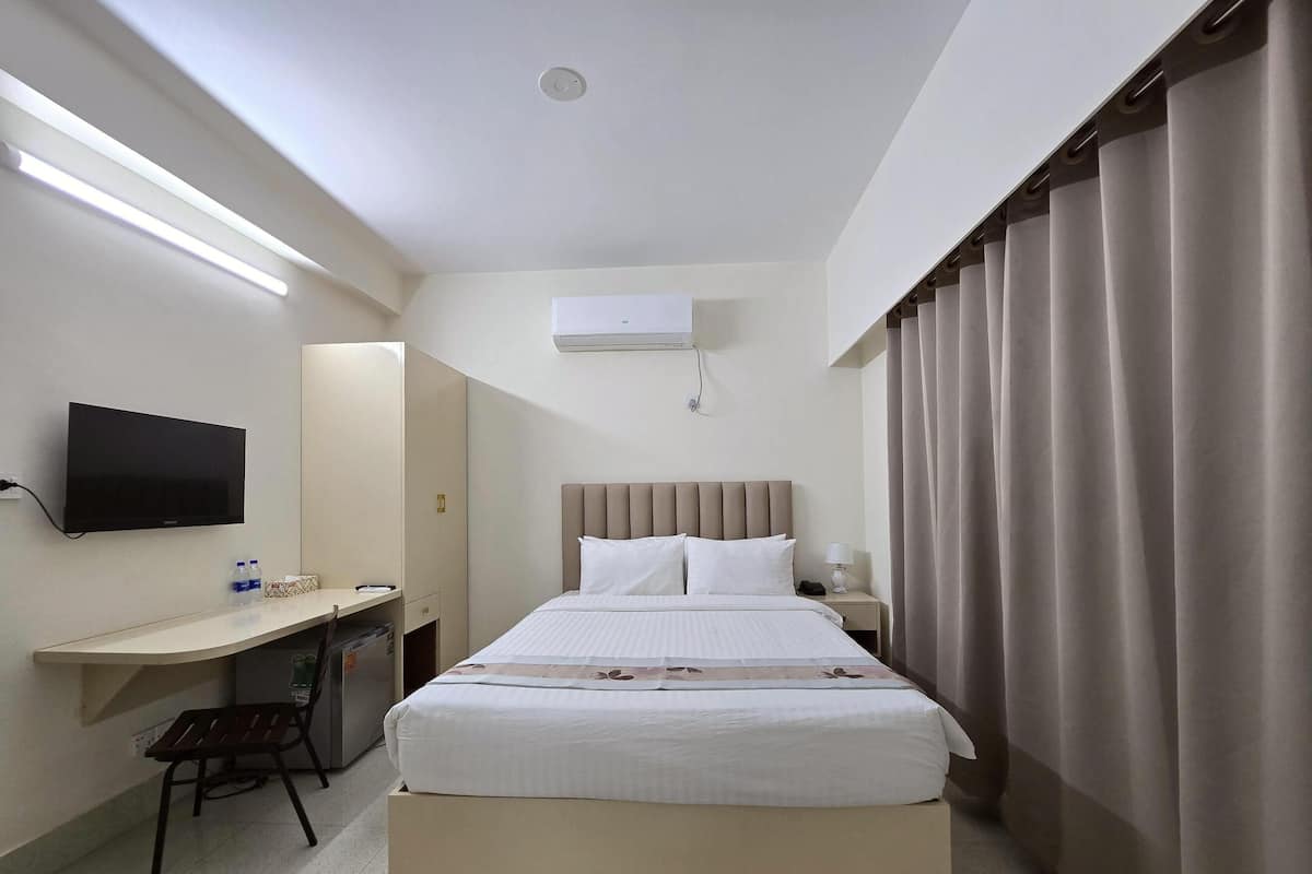 A hotel room with a bed, a desk, a chair, a television, and a window with curtains.
