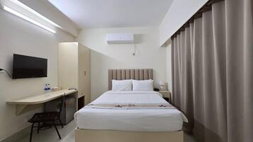 A hotel room with a bed, a desk, a chair, a television, and a window with curtains.